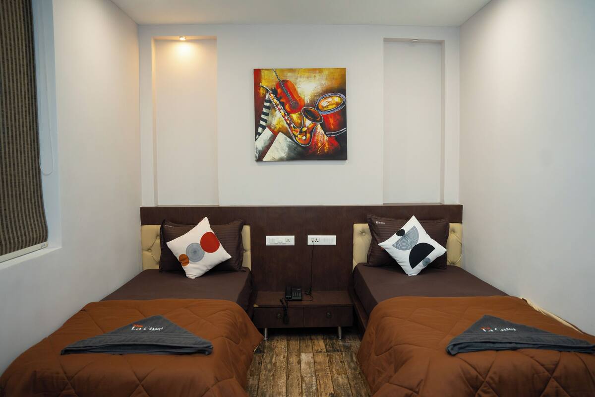 A hotel room with two beds, a painting on the wall, and a small table between the beds.