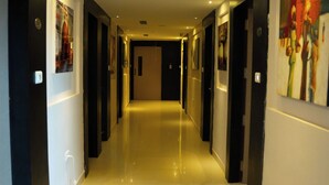 Un couloir d’hôtel long et rectiligne, avec des portes de chaque côté, un éclairage encastré et des œuvres d’art accrochées aux murs.