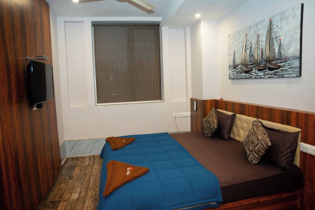 A bedroom with a bed, a painting, a window, and a television.