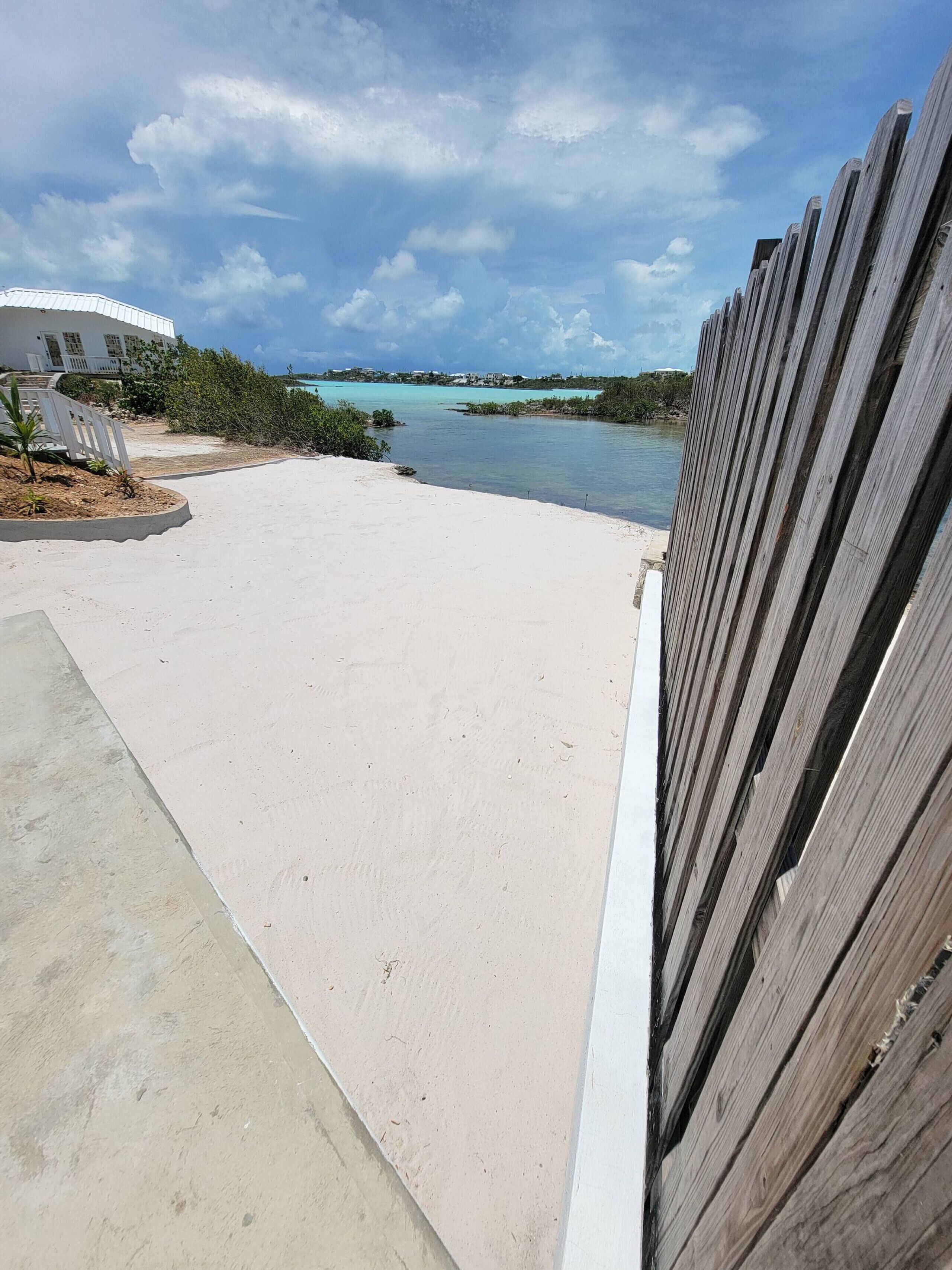 En strand med et træhegn, en betongang og en bygning i baggrunden.