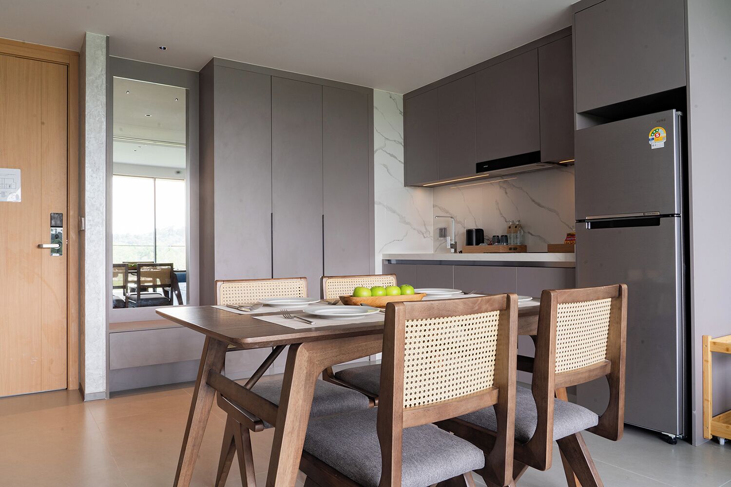 Une cuisine moderne avec des meubles gris, un réfrigérateur en acier inoxydable et une table à manger avec des chaises.