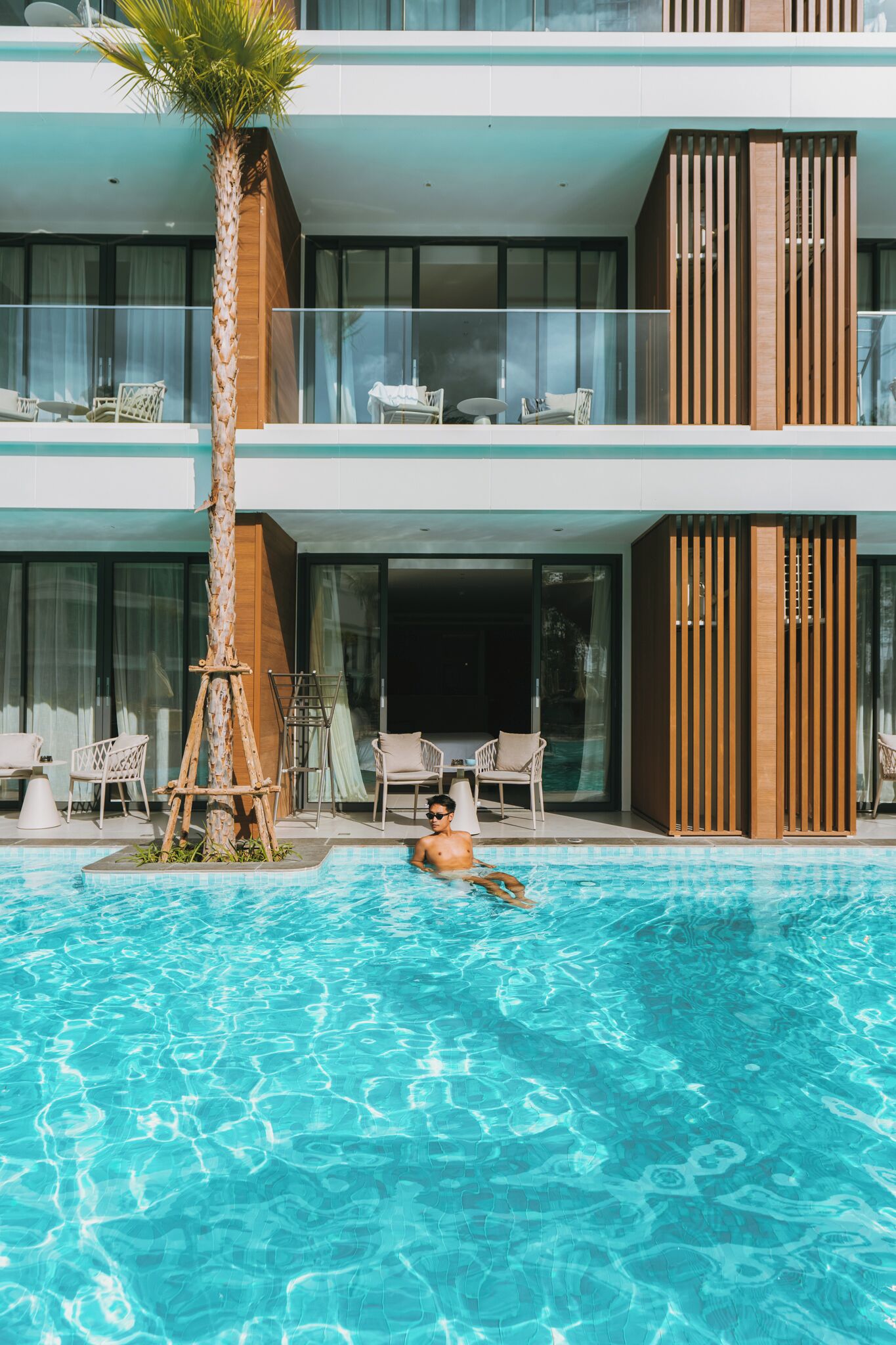 Un hotel moderno con piscina, sillones de descanso y una palmera.