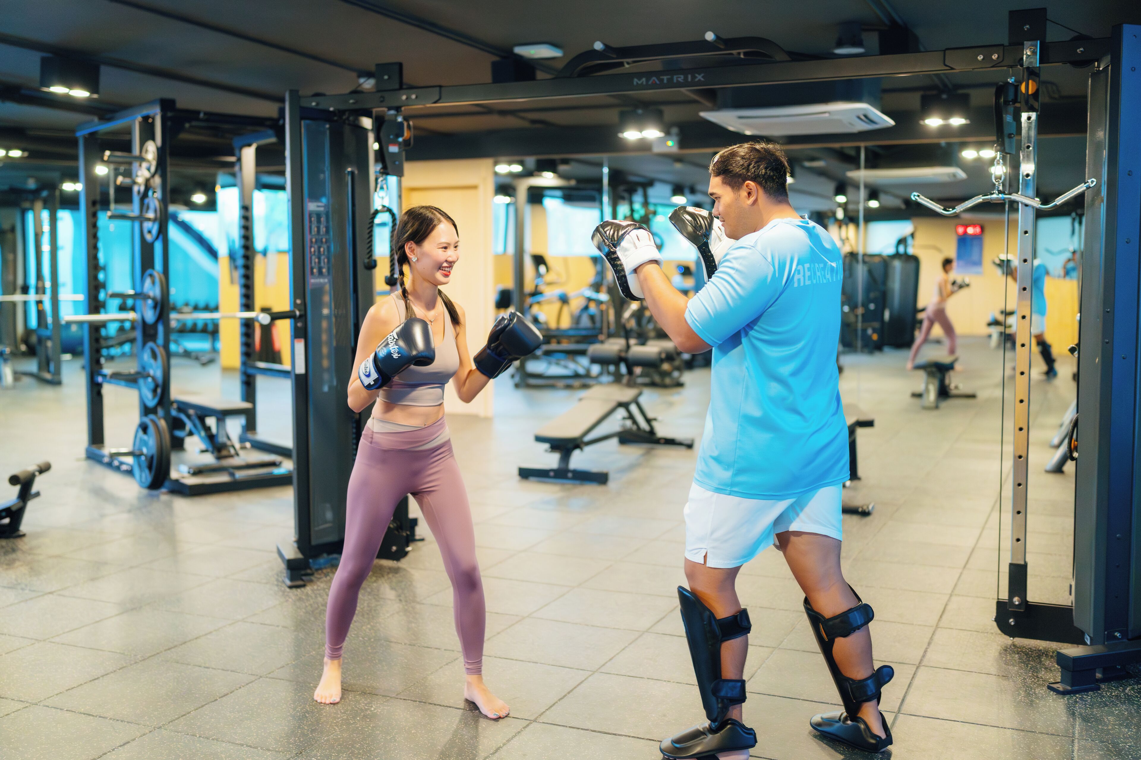 A gym with various exercise equipment and a person practicing boxing.