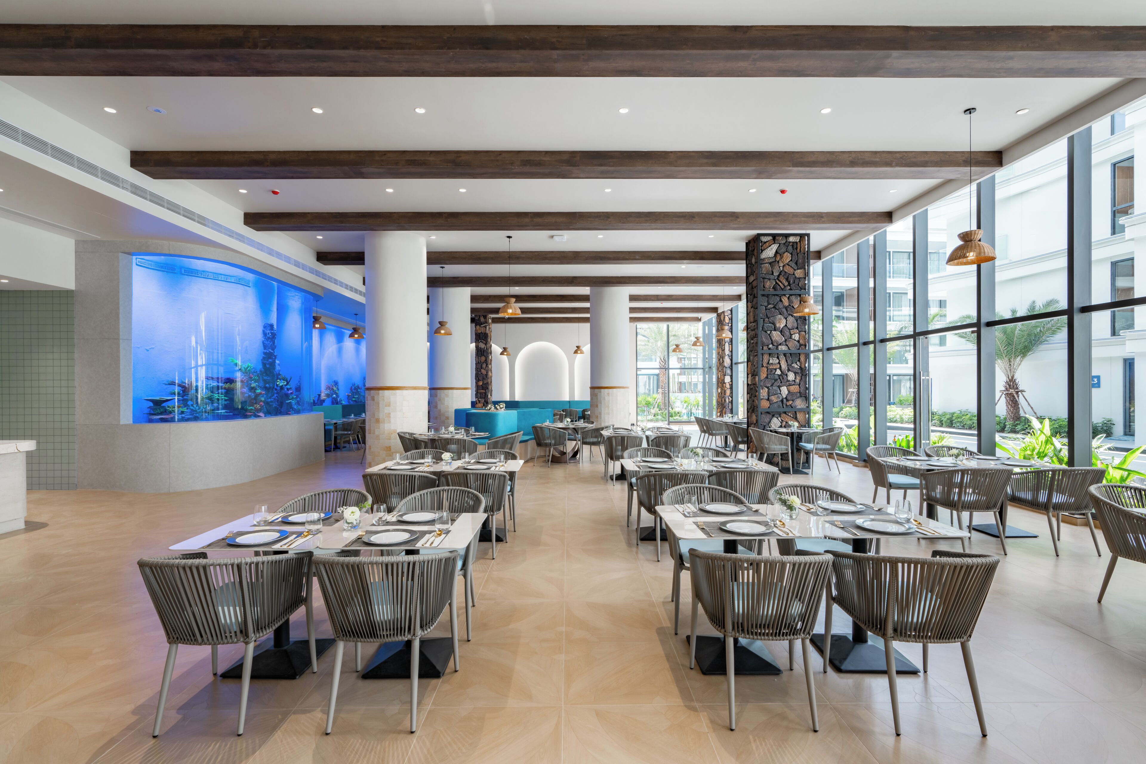 A spacious restaurant with high ceilings, modern lighting, and a large aquarium wall.