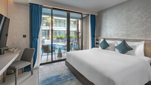 A modern hotel room with a large bed, a desk, and a view of an outdoor pool area. - Kora Beach Resort Phuket (Choeng Thale)