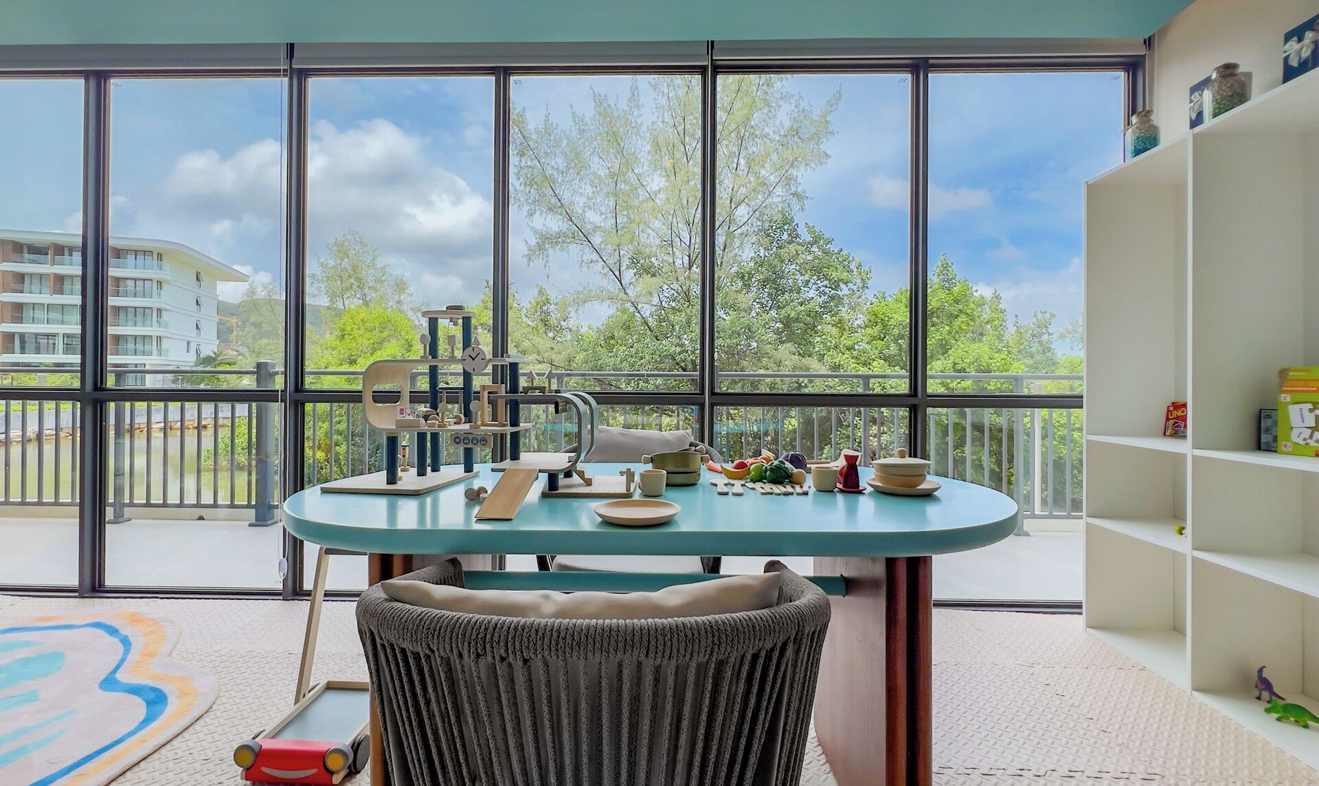 A balcony with a table set for dining, a wicker chair, and a bookshelf.