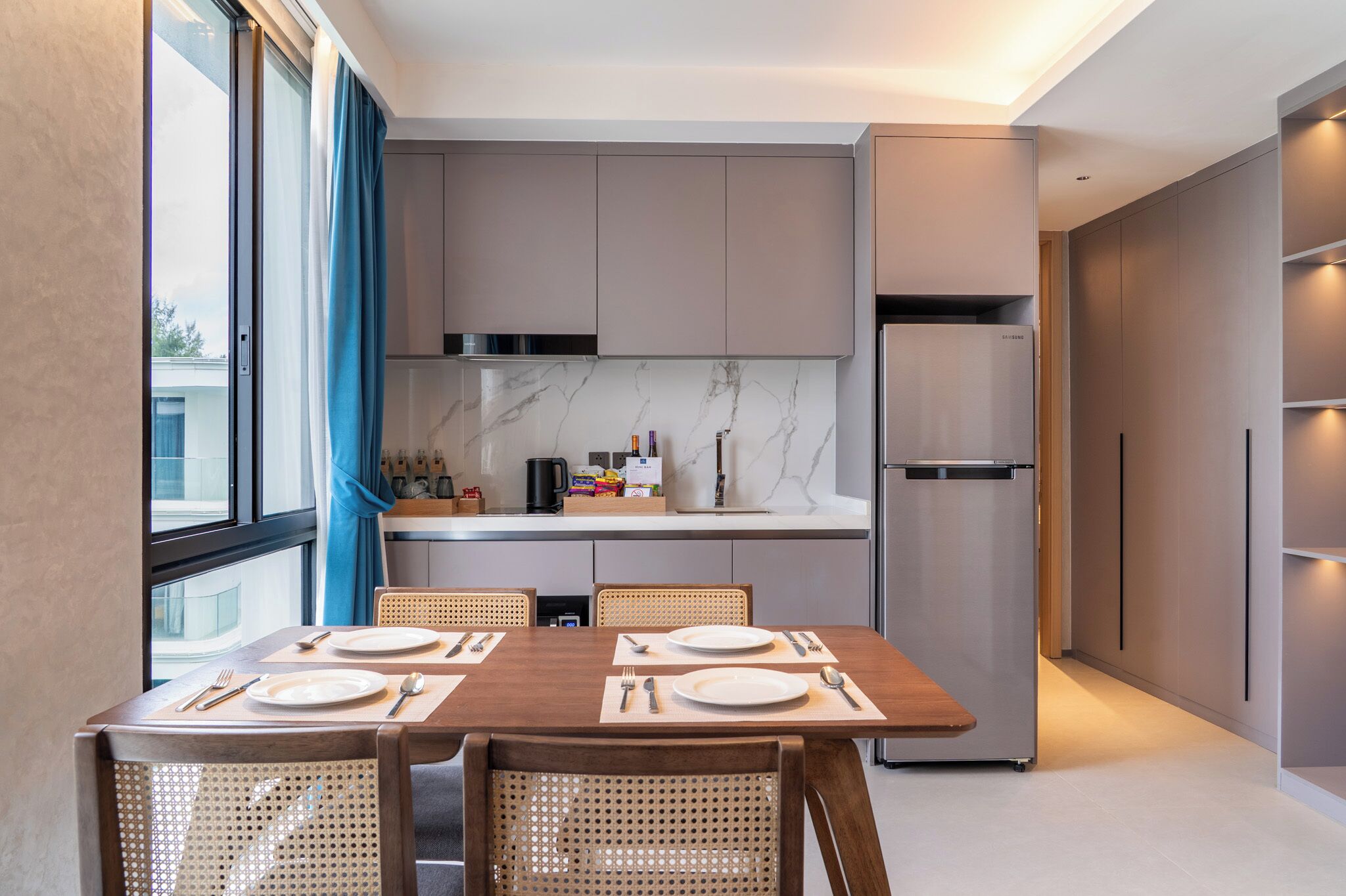 Una cocina moderna con armarios grises, encimera de mármol y comedor con mesa y sillas de madera.