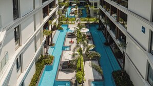 A modern hotel with multiple floors, a central swimming pool, and outdoor seating areas. - Kora Beach Resort Phuket (Choeng Thale)