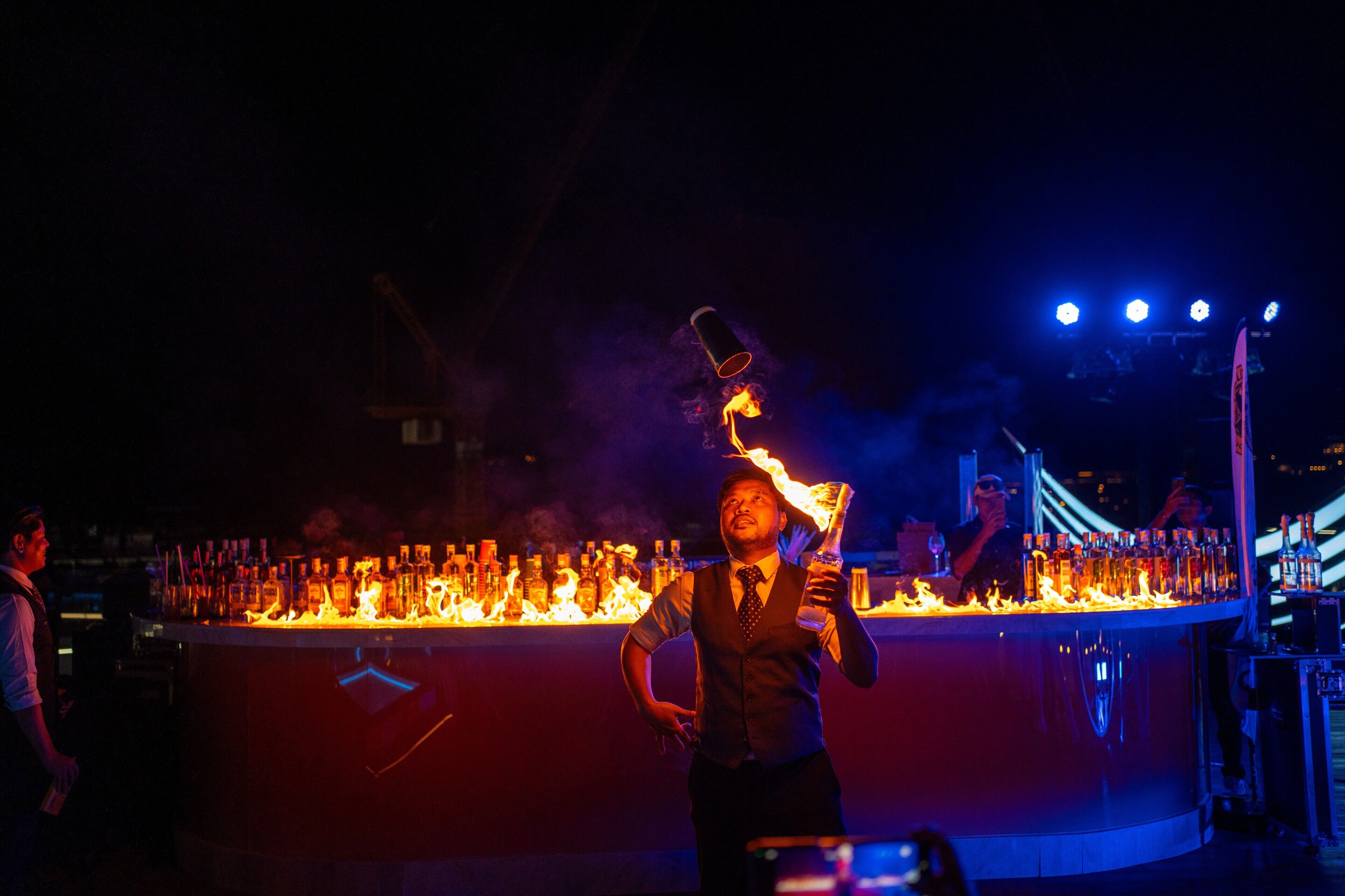 A bar with a flaming bottle and a person performing a trick.
