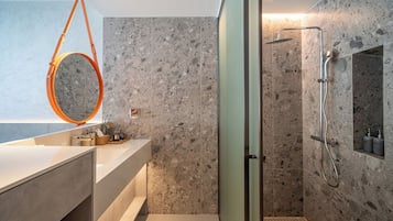 Une salle de bain moderne avec une douche à parois de verre, un mur recouvert de carreaux de marbre et un meuble-lavabo agrémenté d’un miroir rond.
