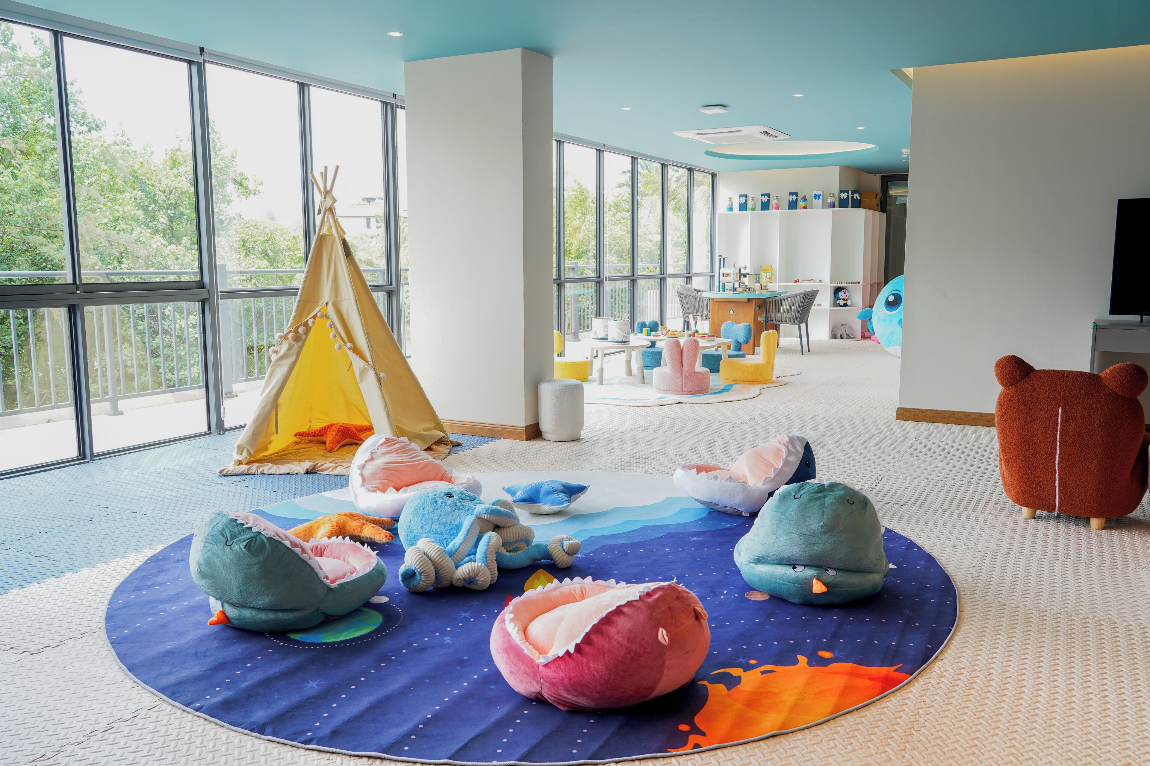 A spacious room with large windows, a play area with colorful cushions and toys, and a tent.