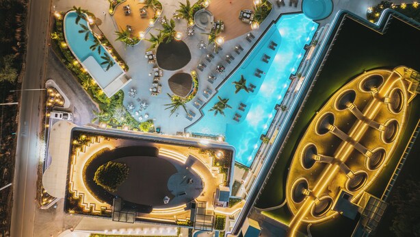 An aerial view of a resort with multiple swimming pools, sun loungers, and a large circular water feature. - Kora Beach Resort Phuket (Choeng Thale)