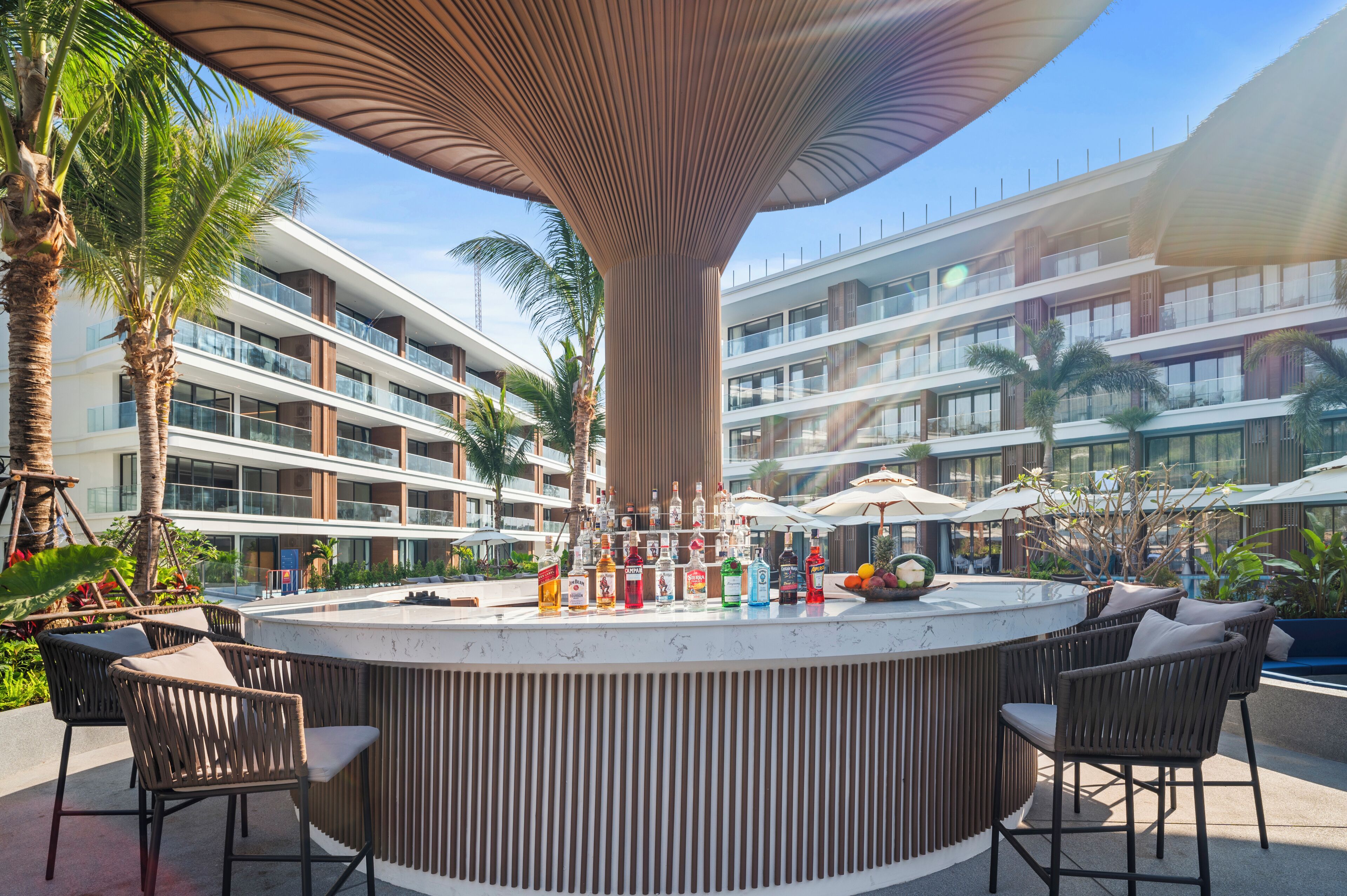 Un área de bar moderna al aire libre, con barra central, asientos y sombrillas.