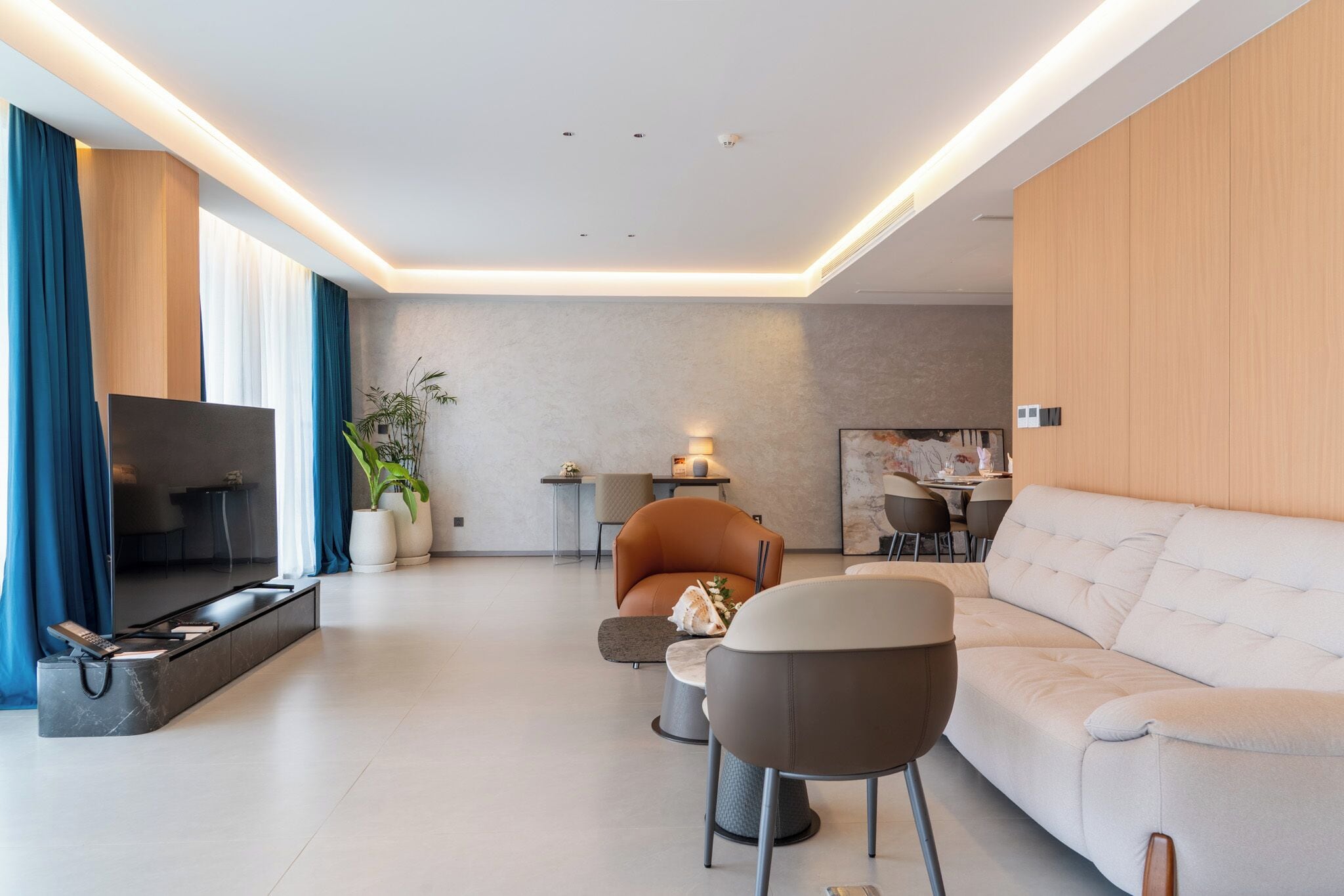 A modern living room with a sofa, armchairs, a TV, and a dining area.