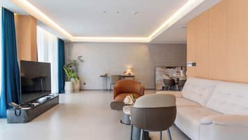 A modern living room with a sofa, armchairs, a TV, and a dining area.