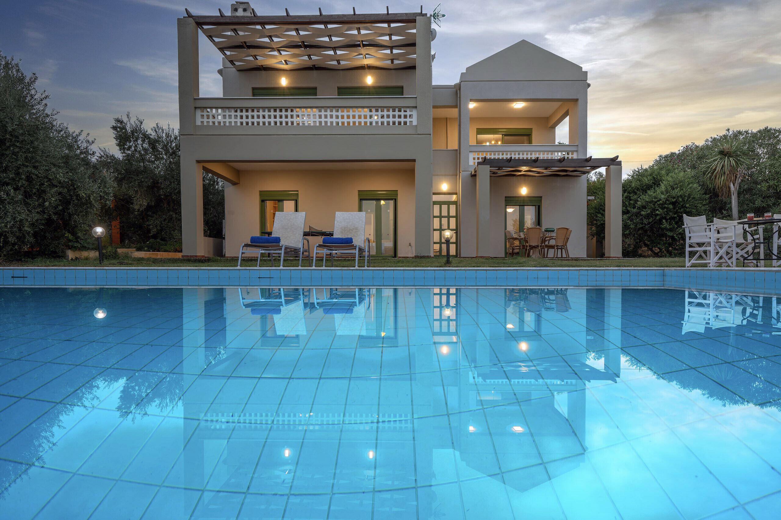Ett modernt hus i två våningar med pool, utomhusmöbler och en pergola.