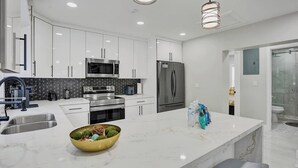 A modern kitchen with white cabinets, stainless steel appliances, and a marble island.