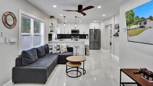 A modern kitchen with white cabinets, stainless steel appliances, and a dining area with a grey sofa and round table.