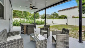 A covered patio area with wicker furniture, a glass-top table, and a ceiling fan.