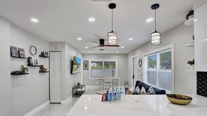 A modern kitchen with a marble island, pendant lights, and a dining area with a view.