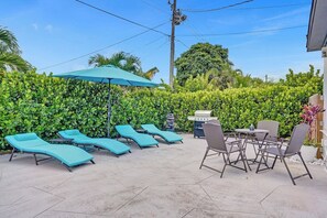 Eine Terrassenanlage mit Liegestühlen, einem Tisch, üppiger Bepflanzung und einem Grill.
