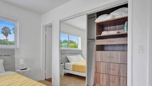 Een slaapkamer met een bed, nachtkastje, kledingkast en een raam met uitzicht op groen.