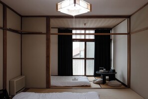 Una habitación tradicional japonesa con suelo de tatami, un futón, una mesita con una lámpara y una puerta corredera que da a un balcón.