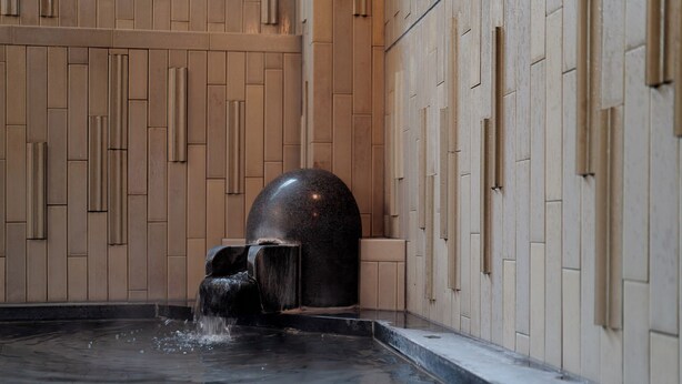 Un espace piscine intérieur moderne, agrémenté d’un élément décoratif aquatique et d’une structure en pierre.