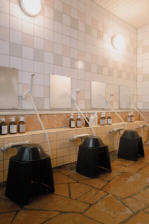 Un baño con paredes de azulejos, varios lavamanos, dispensadores de jabón y reposapiés negros.