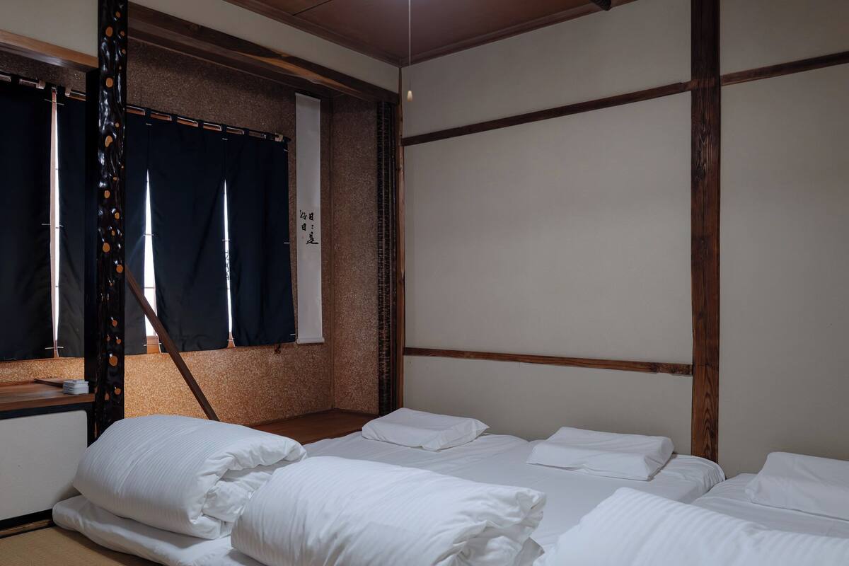 A room with a traditional Japanese-style bed, a wooden headboard, and a window with dark curtains.