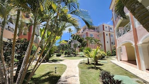 A courtyard with palm trees, a pathway, and buildings with balconies. - Bavaro-El Cortecito Beach Cozy apartment with AC and Fast WiFi. No cleaning fee (Punta Cana)