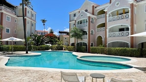 A pool area with a curved design, surrounded by palm trees and a building with balconies. - Bavaro-El Cortecito Beach Cozy apartment with AC and Fast WiFi. No cleaning fee (Punta Cana)