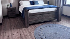 A bedroom with a wooden bed, a ceiling fan, a round rug, and a nightstand with a lamp.
