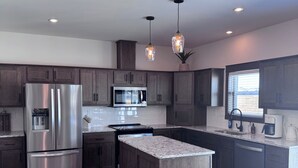A modern kitchen with stainless steel appliances, dark wood cabinets, granite countertops, and pendant lighting.