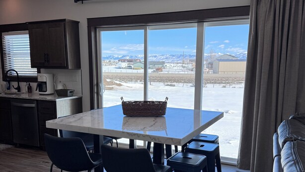 A modern kitchen with a dining area, large windows, and a view of a snowy landscape.