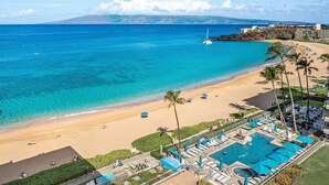 A beach resort with a swimming pool, lounge chairs, and a view of the ocean.
