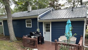Une petite maison avec un porche, un barbecue et un espace salon abrité.