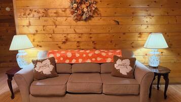 A cozy living room with a wooden wall, a brown sofa, two lamps, and a decorative wreath.