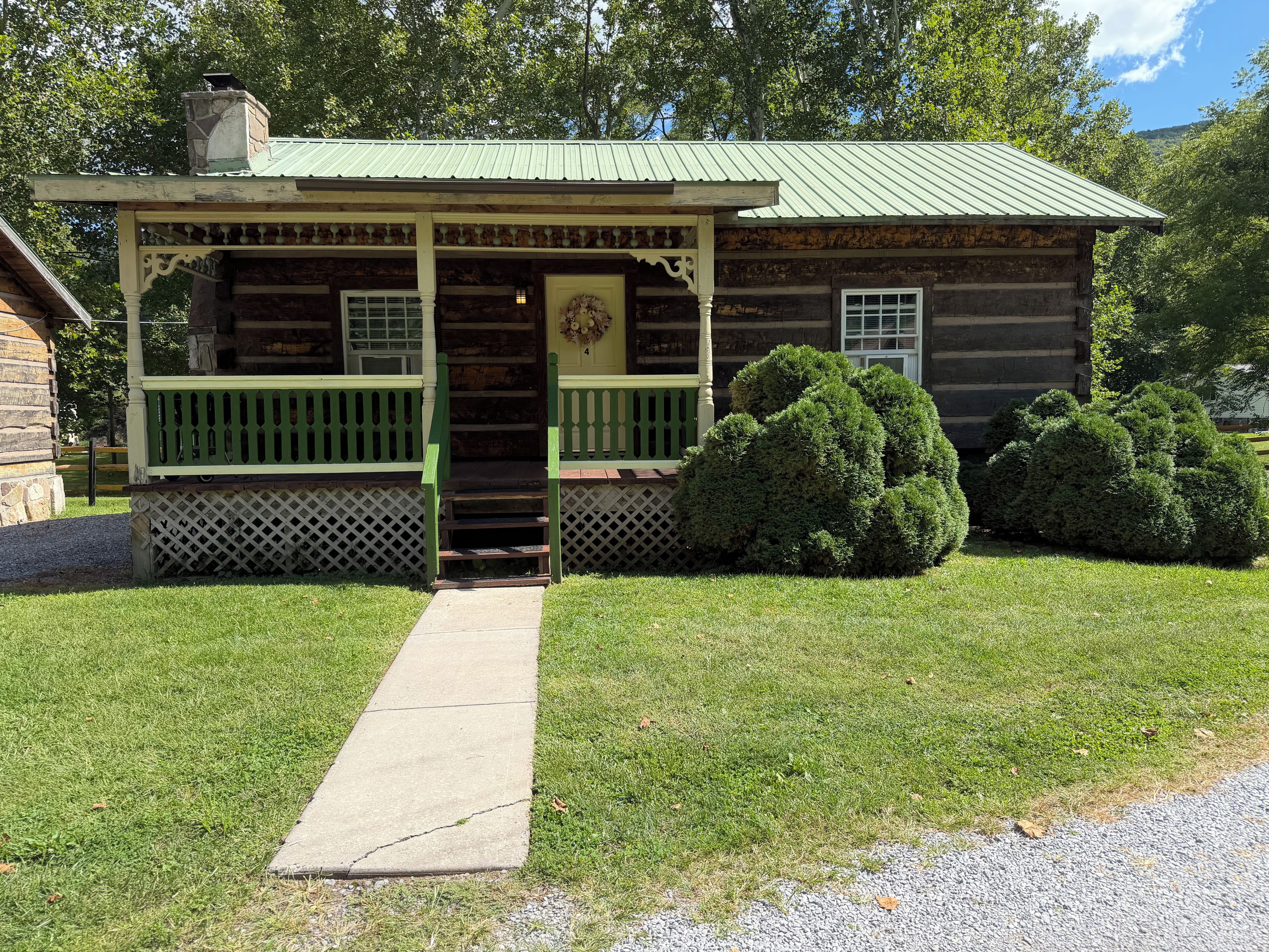 A rustic log cabin with a porch, a chimney, and a well-maintained lawn.