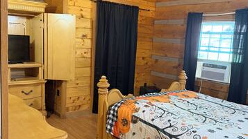 Ein Zimmer in einer Holzhütte mit einem Bett, einem Fernseher, einem Kleiderschrank und einem Fenster mit Vorhängen.