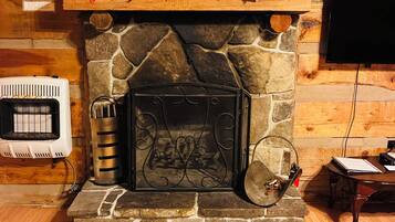 A stone fireplace with a sign above it, a television mounted on the wall, and a small table with a book and a remote control.