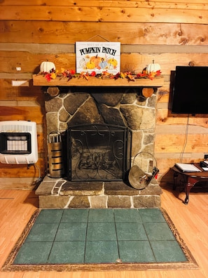 A stone fireplace with a sign above it, a television mounted on the wall, and a small table with a book and a remote control.