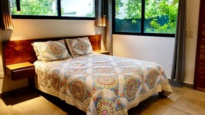 Un dormitorio con una cama grande, dos mesitas de noche y un ventanal con vistas a zonas verdes.