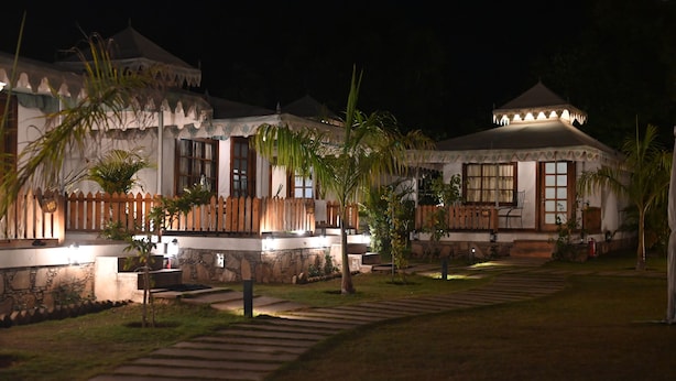 A traditional-style building with a covered patio area, stone walls, and a well-maintained garden with palm trees. - Arvana Resort & Spa Pushkar (Pushkar)
