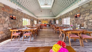 A spacious dining hall with stone walls, wooden tables, and chairs. - Arvana Resort & Spa Pushkar (Pushkar)