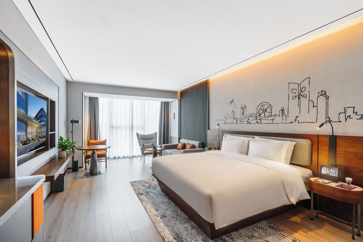 A modern hotel room with a large bed, a desk, a chair, a TV, and a cityscape mural on the wall.