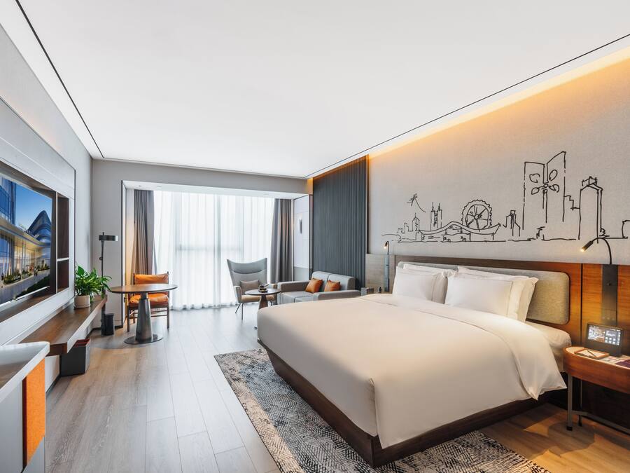 A modern hotel room with a large bed, a desk, a chair, a TV, and a cityscape mural on the wall.