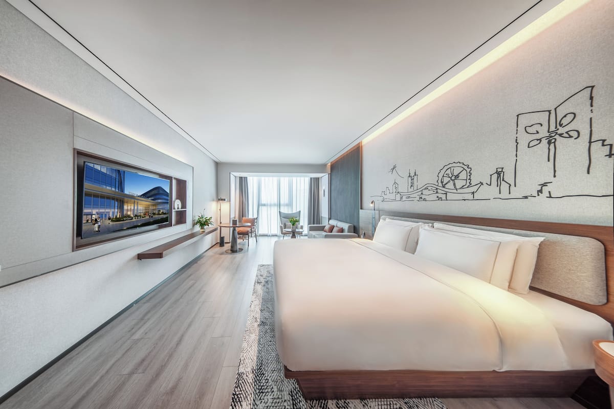 A modern hotel room with a large bed, a television on the wall, and a cityscape mural.