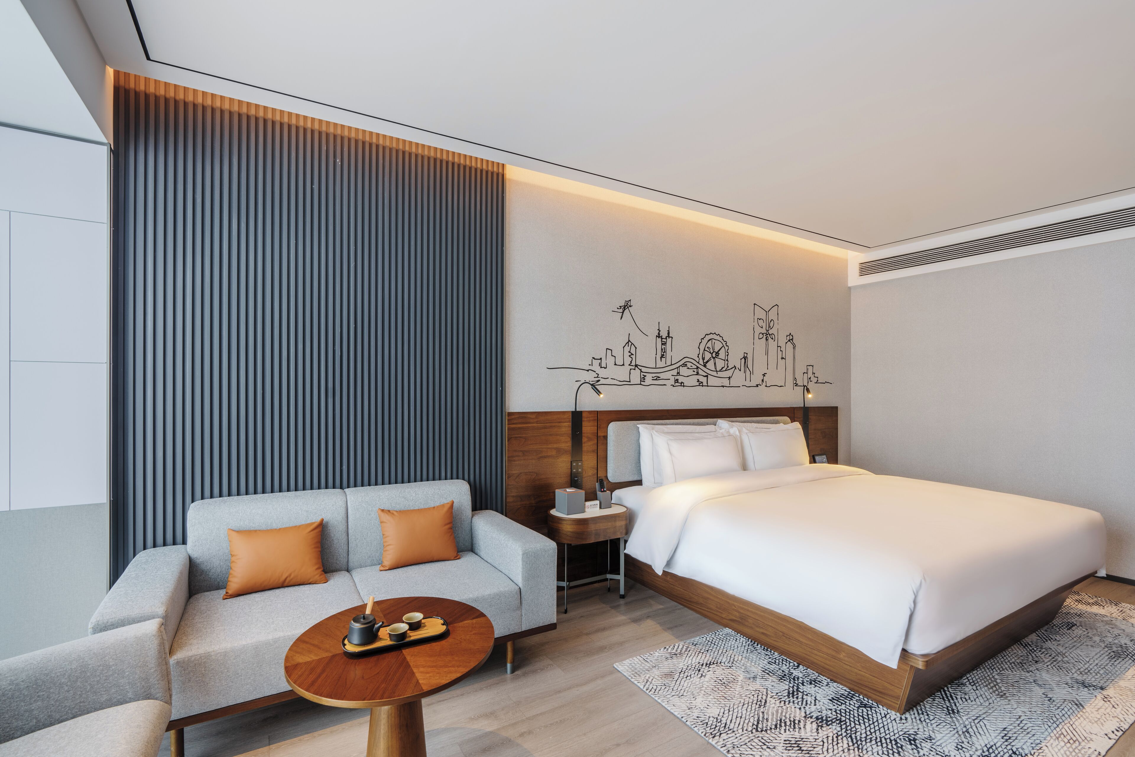 Ein modernes Hotelzimmer mit einer Couch, einem kleinen Tisch, einem Bett und einem dekorativen Wandbild.