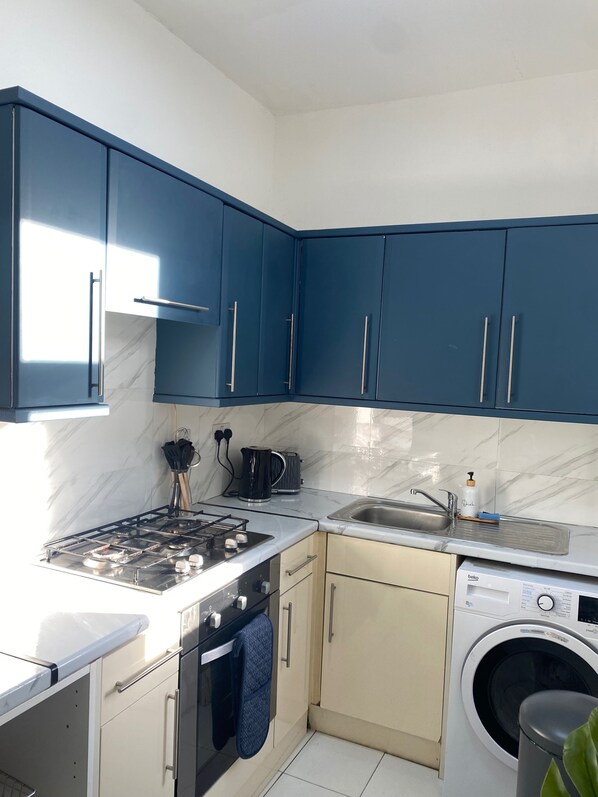 Cocina compacta con armarios azules, estufa a gas, lavabo y lavadora.
